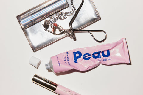 Pink cosmetic tube labeled 'Pink" with eyelash curler and on a white background